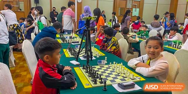 Students intently focused on a game of chess during a tournament or club activity, with a tripod set up to record the match at The British International School Shanghai, Puxi.