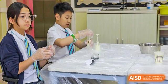 A student in school uniform carefully mixing ingredients for a science experiment or craft project in a classroom setting at The British International School Shanghai, Puxi.