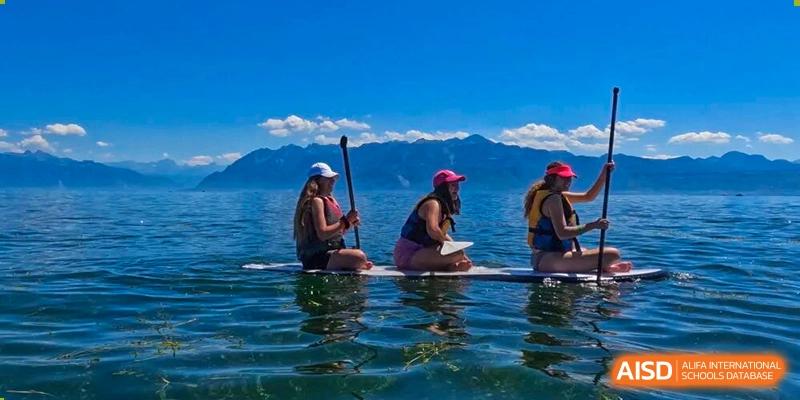 A group of people enjoying paddleboarding on calm water, with scenic mountains in the background, a school trip activity at The British International School Shanghai, Puxi.