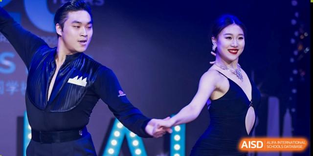 The lower half of two people's bodies as they hold hands while engaged in a choreographed dance performance in a dimly lit setting at The British International School Shanghai, Puxi.