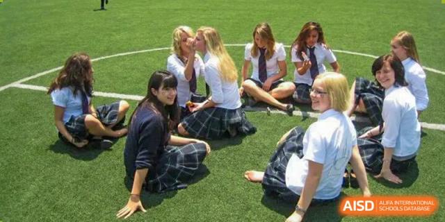 A group of female students wearing school uniforms sitting in a circle on a grassy field, chatting and relaxing during a break at The British International School Shanghai, Puxi.