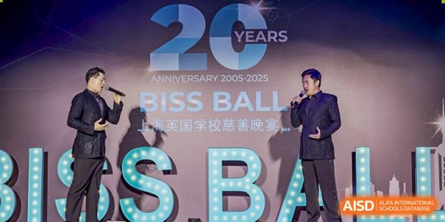A man in a suit is speaking on stage next to large, illuminated letters reading "SBA" during an event at The British International School Shanghai, Puxi.