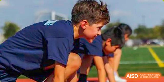 Young students in navy shirts are focused and crouched in the starting blocks, ready for a race at The British International School Shanghai, Puxi.