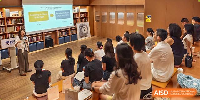 Students sit on the floor in a bright, wood-paneled room, attentively facing a presentation screen in a classroom setting, Avenues: The World School.