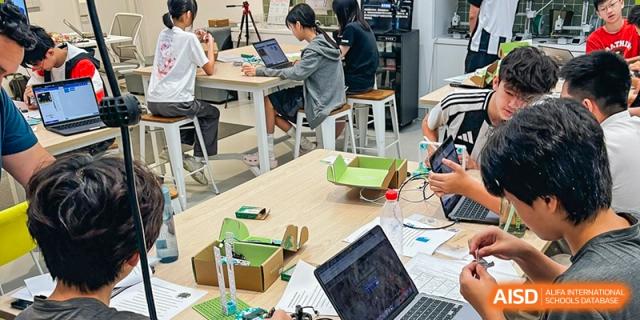 Students work individually on laptops and with physical models, possibly doing a technology or engineering project in a bright workshop space, Avenues: The World School.