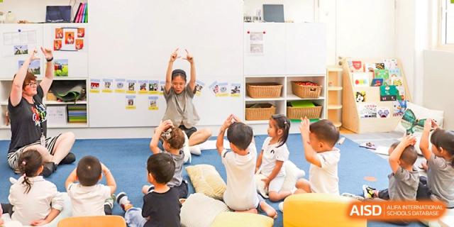 An adult leads a group of young students in a fun, dynamic indoor activity or exercise class on a bright blue mat, Avenues: The World School.