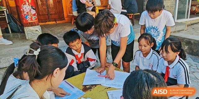 A group of students huddle around a table, actively collaborating or looking at papers for a class activity or project, Avenues: The World School.