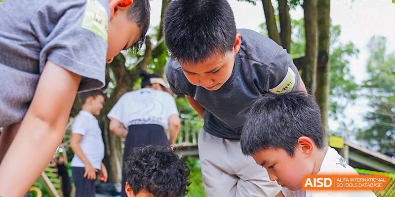 A group of students outdoors, gathered closely while looking down at an activity or task, possibly during a field trip, Avenues: The World School.