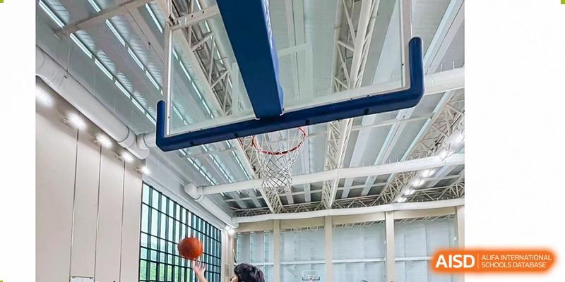 A basketball hangs momentarily in the hoop of an indoor court, indicating a game or practice is taking place, Avenues: The World School.