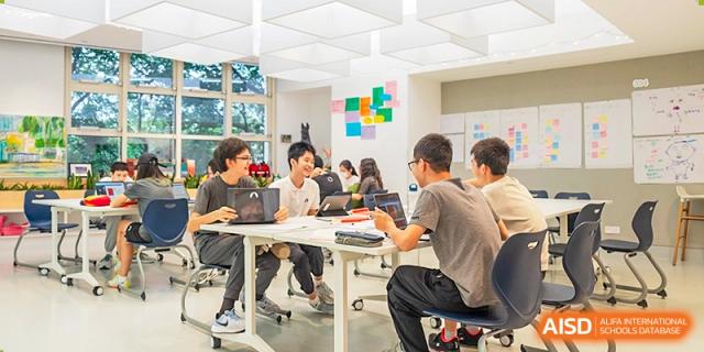 Students working collaboratively on laptops and in discussion around white tables in a bright, modern, and flexible classroom space, Avenues: The World School.