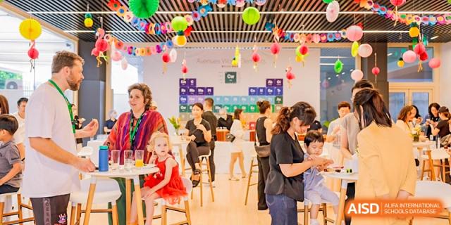 A casual gathering or party indoors with adults and children seated at tables decorated with balloons, Avenues: The World School.