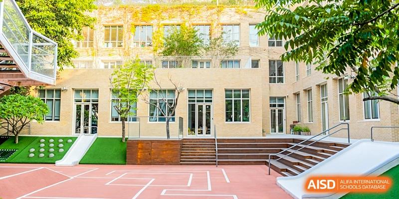 An outdoor basketball or play court situated between two modern school buildings with a lush tree visible, Avenues: The World School.  Middle Row (Left to Right)