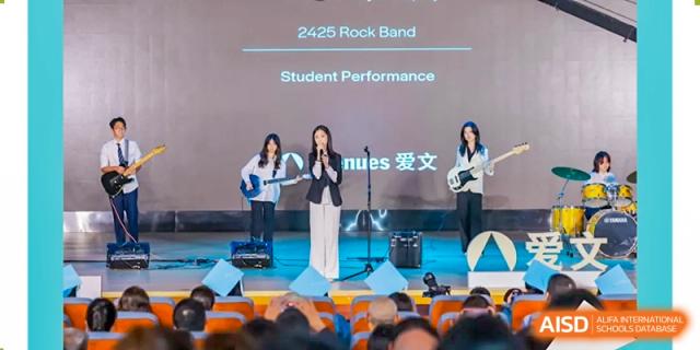 Female students performing a song on stage under the banner "2425 Rock Band Student Performance" to an audience, Avenues: The World School.
