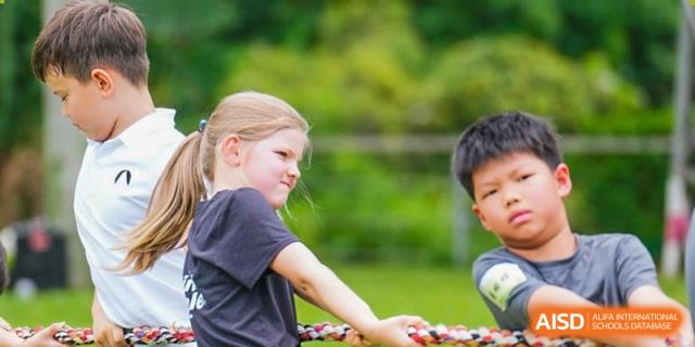 A young blonde girl participates in an outdoor tug-of-war game, pulling with focused effort alongside other children, Avenues: The World School.