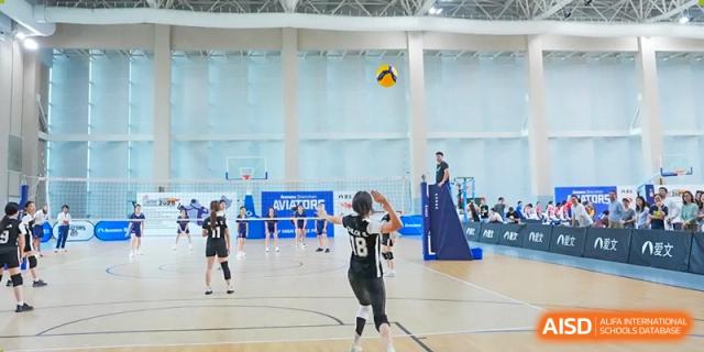 A student in a black and white uniform prepares to bump or set a volleyball during a match on a light-colored indoor court, Avenues: The World School.