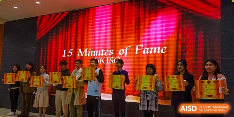 Students stand on a stage lit with red lights during a "15 Minutes of Fame" performance at International Studies Center Of Chongqing Nankai Secondary School.