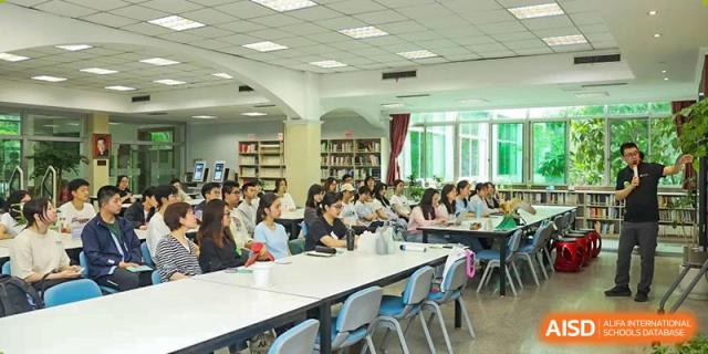 Students sit at long white tables in a large, well-lit library for a study session at International Studies Center Of Chongqing Nankai Secondary School.