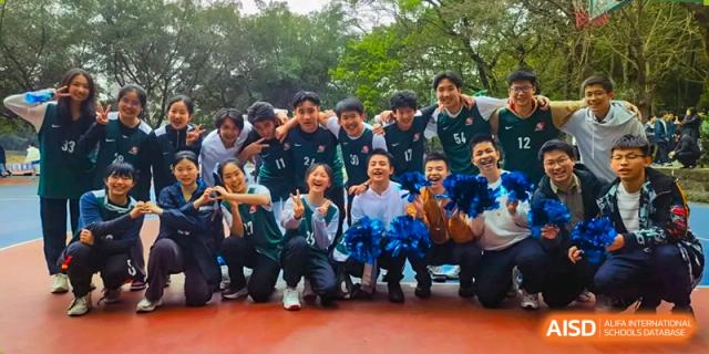 A group of students in dark sports uniforms cheers and poses together on an outdoor court at International Studies Center Of Chongqing Nankai Secondary School.