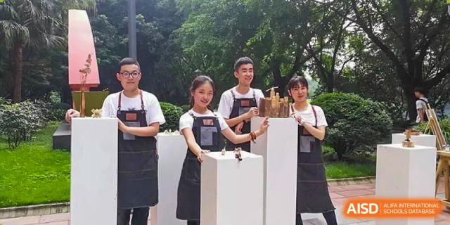 Four students in matching aprons stand behind white pedestals during a creative workshop at International Studies Center Of Chongqing Nankai Secondary School.