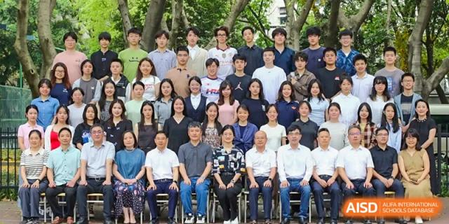 A large group of students and faculty members poses for a formal group portrait outdoors at International Studies Center Of Chongqing Nankai Secondary School.