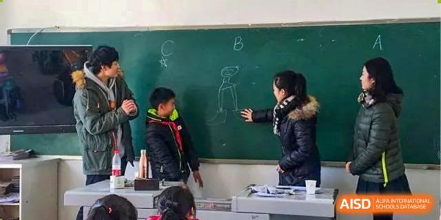 A teacher uses a chalkboard to explain a concept to a young student in a classroom at International Studies Center Of Chongqing Nankai Secondary School.