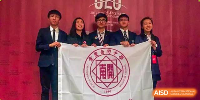 Students in formal blazers pose behind a large white school flag during a ceremony at International Studies Center Of Chongqing Nankai Secondary School.