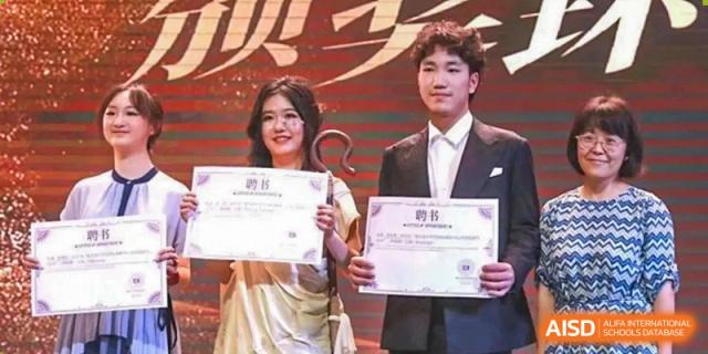 Two students in formal wear stand on a stage holding award certificates during a celebratory school event at International Studies Center Of Chongqing Nankai Secondary School.