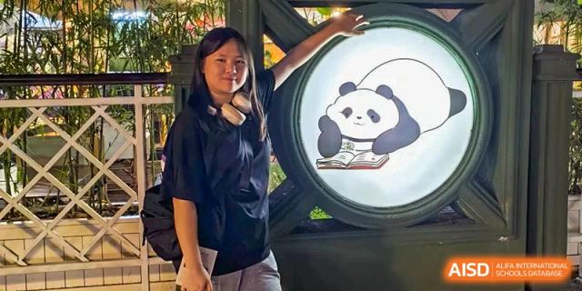 A student poses next to a circular sign featuring a panda illustration on campus at International Studies Center Of Chongqing Nankai Secondary School.