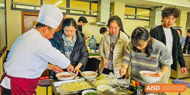 Students and a chef work together in a kitchen to prepare traditional dumplings during a culinary workshop at International Studies Center Of Chongqing Nankai Secondary School.