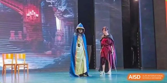 Two performers in dramatic blue and red capes act out a scene on a stage with a digital backdrop at International Studies Center Of Chongqing Nankai Secondary School.