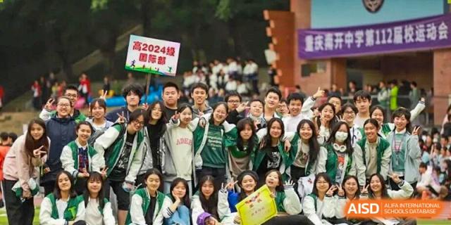 A large, enthusiastic group of students in green and white jackets gathers for a commemorative photo during a 2024 campus event at International Studies Center Of Chongqing Nankai Secondary School.