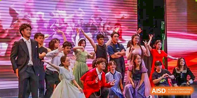 A group of students in vibrant costumes performs an expressive theatrical dance routine on a stage with a digital backdrop at International Studies Center Of Chongqing Nankai Secondary School.