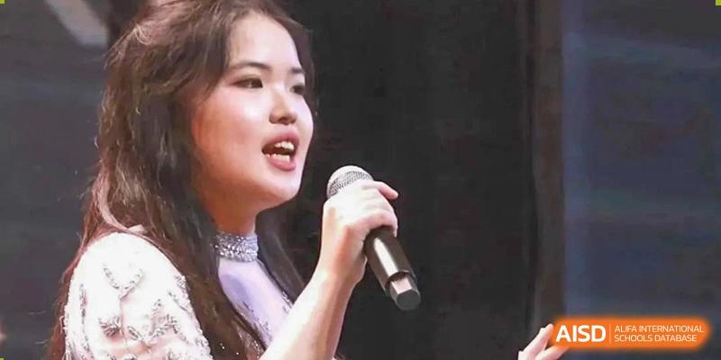 A student with a focused expression holds a microphone and delivers a speech or musical performance during a formal school assembly at International Studies Center Of Chongqing Nankai Secondary School.