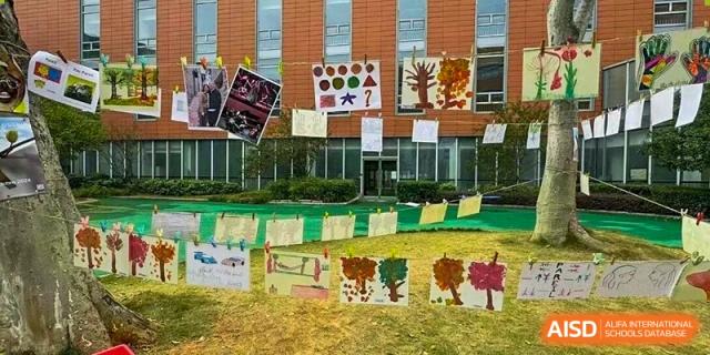 Colorful children's paintings hanging on a clothesline in the school courtyard with the brick building in the background at Ecole Française Internationale de Wuhan.