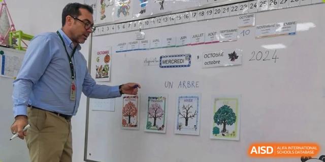 A teacher pointing to a French language calendar and seasonal tree illustrations on a white board in a classroom at Ecole Française Internationale de Wuhan.