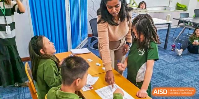 An educator leaning over a desk to provide one-on-one guidance to a student working on a classroom assignment at Ecole Française Internationale de Wuhan.