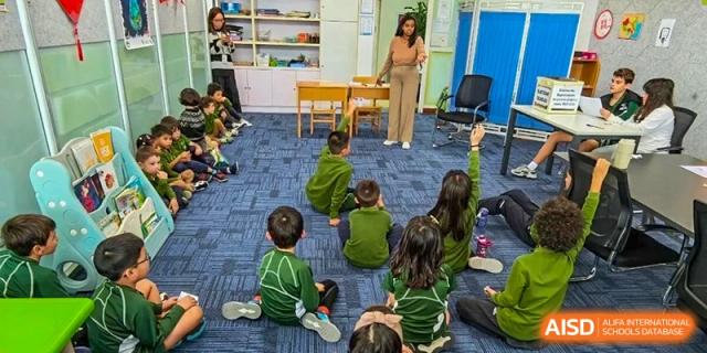 A teacher standing before a class of students seated on a blue carpet, encouraging participation and questions at Ecole Française Internationale de Wuhan.