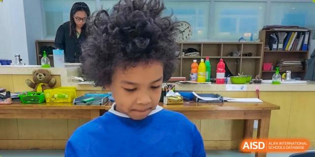 A close-up photo of a young student with curly hair in a classroom setting with art supplies visible in the background at Ecole Française Internationale de Wuhan.