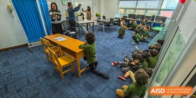 Students sit on a blue rug while a teacher stands at the front of a modern classroom to lead a group discussion at Ecole Française Internationale de Wuhan.