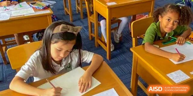 A young girl with a headband sits at her wooden desk, carefully practicing her writing during a morning lesson at Ecole Française Internationale de Wuhan.