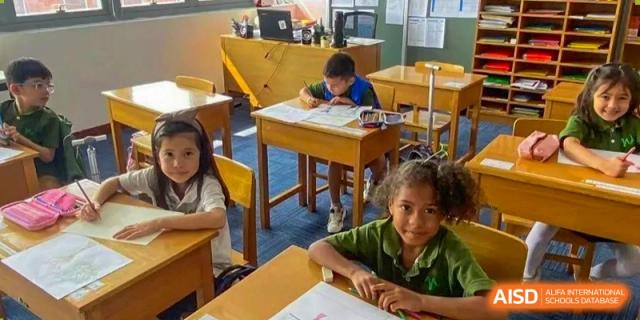 Students seated at wooden desks in a sunlit classroom working quietly on their individual writing assignments at Ecole Française Internationale de Wuhan.