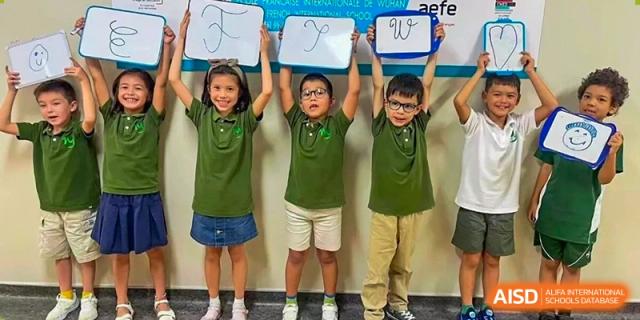 Three students smiling while holding up whiteboards displaying the letters F, I, and W at Ecole Française Internationale de Wuhan.