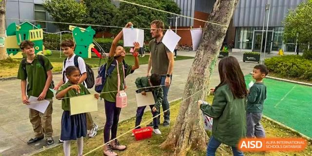 Students and a teacher hanging papers on a string tied to a tree in the school garden at Ecole Française Internationale de Wuhan.