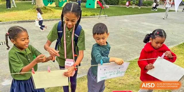 Two students working together to clip their drawings onto a clothesline in the outdoor play area at Ecole Française Internationale de Wuhan.