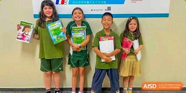 Four young students in green uniforms holding up their colorful workbooks and smiling at Ecole Française Internationale de Wuhan.