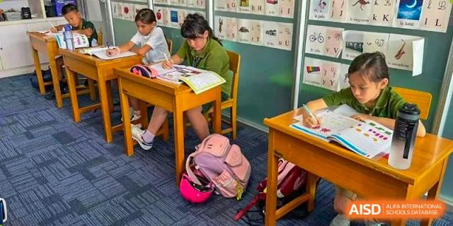 A student sitting at a wooden desk with a pink backpack nearby, diligently working on an assignment at Ecole Française Internationale de Wuhan.