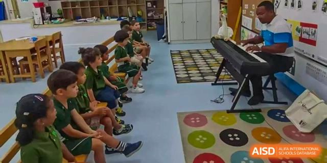 A row of students sitting on a bench during a music lesson near a piano and colorful rugs at Ecole Française Internationale de Wuhan.