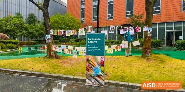 An outdoor art installation featuring a green sign and drawings hanging on lines in the grass at Ecole Française Internationale de Wuhan.