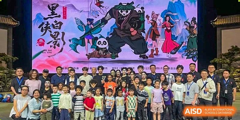 A large group of students and adults pose together in front of a colorful animated backdrop during an event at Ecole Française Internationale de Wuhan.