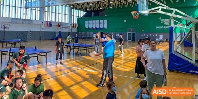 Students and instructors engage in physical education activities inside a bright, sunlit gymnasium at Ecole Française Internationale de Wuhan.